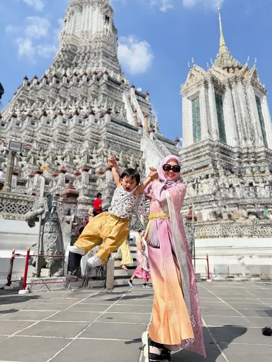 Ria Ricis dan Moana kini sedang berlibur ke Thailand, terlihat Ria mengenakan baju tradisional Thailand warna pink. Dan Moana dengan atasan bermotif dipadukan celana kuning. [@riaricis1795]