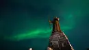 Fenomena yang menciptakan pemandangan alam yang memukau ini adalah Aurora Borealis atau cahaya utara. Tampak dalam foto, Aurora Borealis menerangi langit malam di atas patung Hans Egede yang menghadap Nuuk, Greenland, pada 23 Januari 2026. (Jonathan NACKSTRAND/AFP)