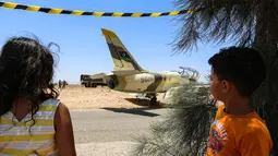 Dua anak melihat kondisi pesawat jet tempur Libya L-39 Albatros pasukan Khalifa Haftar di Kota Medenine di perbatasan Tunisia-Libya (22/7/2019). Jet tempur yang sedang melakukan misi pengintaian dan patroli itu mengalami masalah teknis yang mengakibatkan pendaratan darurat di jalan raya. (AFP Photo/