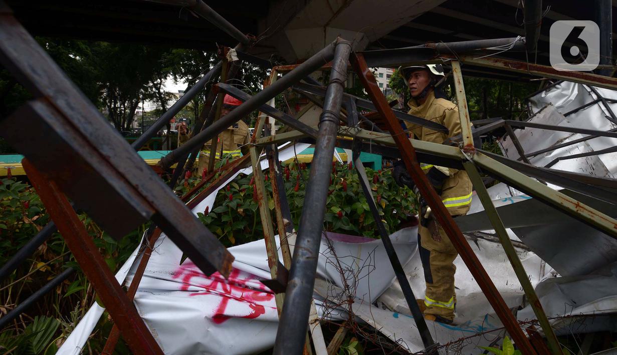 Petugas pemadam kebakaran memotong rangka reklame yang roboh di Jalan Soepomo, Jakarta, Sabtu (28/5/2022). Hujan disertai angin kencang pada pagi tadi membuat papan reklame roboh sehingga membuat kemacetan arus lalu lintas di jalan tersebut. (merdeka.com/Imam Buhori)