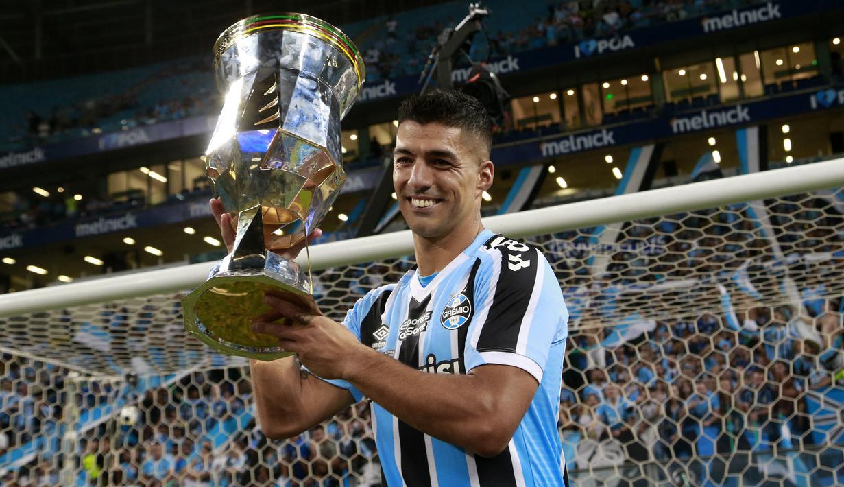 Selebrasi striker Gremio, Luis Suarez dengan trofi juara setelah mengalahkan Caxias pada laga leg kedua final Gaucho Championship di Arena do Gremio Stadium, Porto Alegre, Brasil (8/4/2023). Luis Suarez yang pernah menjadi rekan Lionel Messi di Barcelona saat ini tengah membela Gremio sejak Januari 2023 dan terikat kontrak hingga Desember 2024. Kembali bermain bersama Messi di Inter Miami tentu menjadi nostalgia indah bagi Luis Suarez. (AFP/Silvio Avila)
