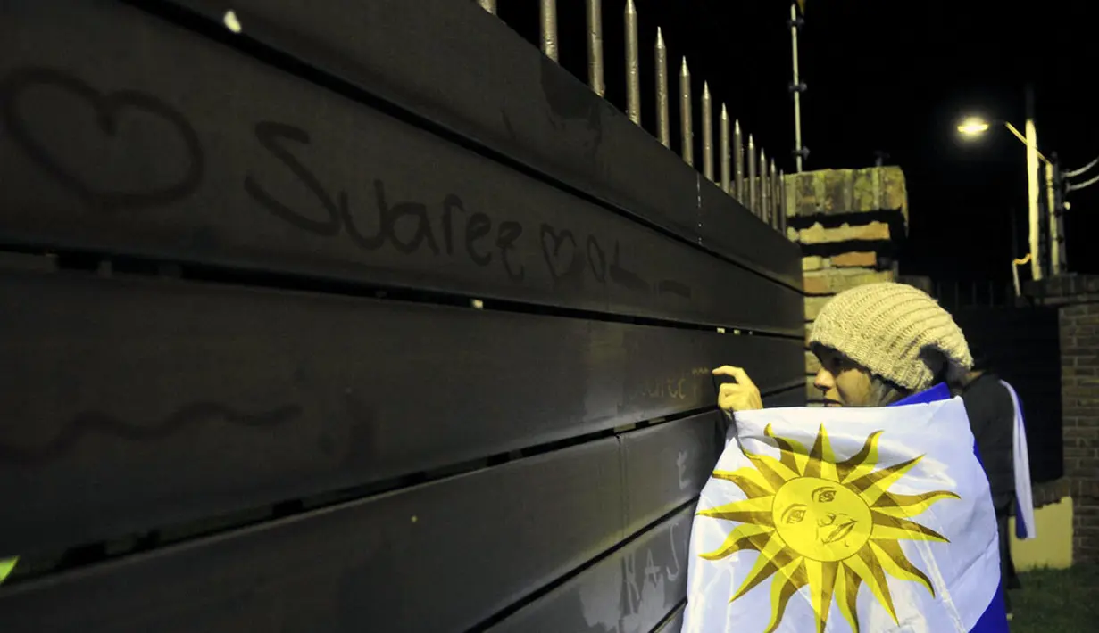 Berbalut bendera kebangsaan Uruguay, salah satu suporter menuliskan nama Luis Suarez di pagar Bandara Montevideo, Carrasco, (26/6/2014). (REUTERS/Carlos Pazos) 
