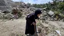 Seorang wanita lanjut usia berjalan melewati petugas pertahanan sipil Lebanon yang sedang mencari korban di antara reruntuhan, sehari setelah serangan Israel di desa Deir Qanun al-Nahr, Lebanon Selatan, pada Rabu 20 Mei 2026. (KAWNAT HAJU/AFP)