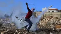 Pengunjuk rasa Palestina menggunakan ketapel untuk mengembalikan tabung gas air mata saat bentrok dengan pasukan keamanan Israel di Desa Kfar Qaddum, dekat pemukiman Yahudi Kedumim, Tepi Barat, 10 Desember 2021. Pengunjuk rasa memprotes pengambilalihan tanah oleh Israel. (Jaafar ASHTIYEH/AFP)