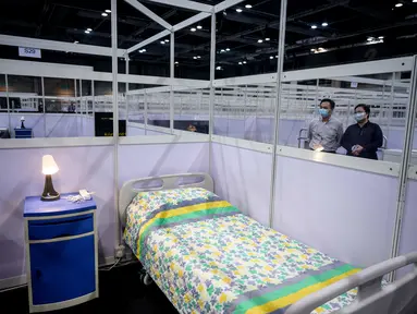 Petugas berdiri di sebelah dinding pemisah antara kamar-kamar yang dipartisi di fasilitas perawatan kesehatan masyarakat di AsiaWorld-Expo di Hong Kong, Selasa (24/11/2020). Rumah sakit darurat khusus corona itu kembali dibuka menyusul lonjakan kasus COVID-19 di Hong Kong. (Anthony WALLACE/AFP)