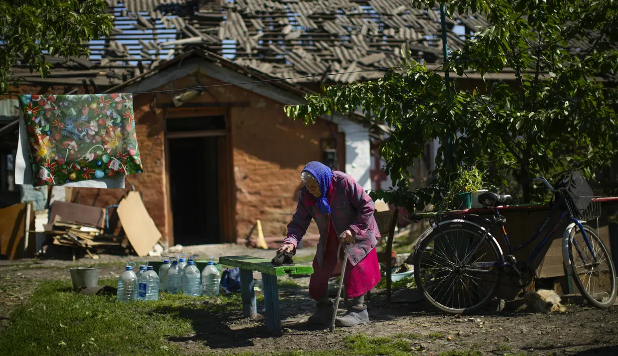 <p>Penduduk lokal Valeria membersihkan debu dari bangku di luar rumahnya yang rusak parah, latar belakang, setelah serangan Rusia di Pokrovsk, Ukraina timur, Rabu (25/5/2022). Dua roket menghantam kota Pokrovsk, di wilayah Donetsk pada Rabu pagi, menyebabkan sedikitnya empat cedera. (AP Photo/Francisco Seco)</p>