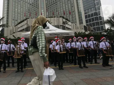 Seorang wanita berjalan di depan para peserta yang sedang bermain angklung saat acara Christmas in Jakarta di Bundaran Hotel Indonesia, Jakarta, Selasa (21/12/2021). Pemerintah Provinsi DKI Jakarta menggelar Christmas in Jakarta dalam rangka menyambut Natal 2021. (Liputan6.com/Johan Tallo)