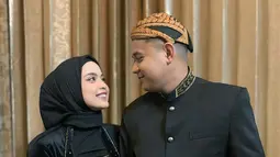 Pedangdut berusia 20 tahun itu tampil elegan dengan kebaya hitamnya, beserta hijab warna senada. Sementara itu, sang suami tampil gagah kenakan beskap dan blangkon. Keduanya tetap serasi dengan perpaduan bawahan kain batik, meski berbeda motif. (Liputan6.com/IG/@putriisnari3)