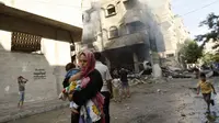 Beberapa warga Palestina berhamburan keluar rumah akibat serangan udara Israel di Gaza, (10/8/2014). Sambil menggendong anak, salah satu warga berlarian menghindari bangunan yang terbakar. (REUTERS/Ahmed Zakot)