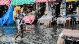 Seorang penjual sapu berjalan melewati banjir di tengah hujan deras yang tiba-tiba mengguyur di sebuah pasar dekorasi Natal di Manila, Filipina (9/12/2020). (Xinhua/Rouelle Umali)