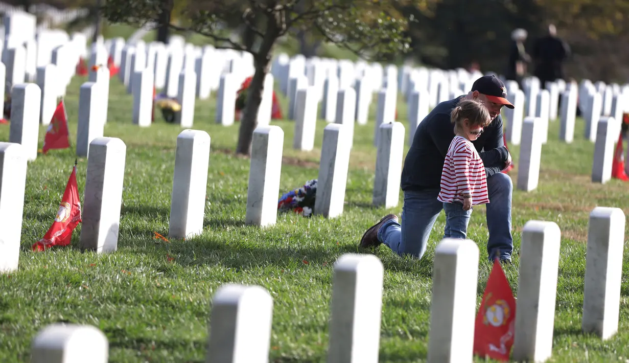 Kip Hogan didampingi putrinya mengunjungi makam temannya Army Gunnery Sgt. Terry Ball saat peringatan Hari Veteran, Arlington, Virginia, AS, Senin (11/11/2019). Rakyat AS memperingati Hari Veteran untuk menghormati mereka yang pernah bertugas di militer AS. (Alex Wong/Getty Images/AFP)