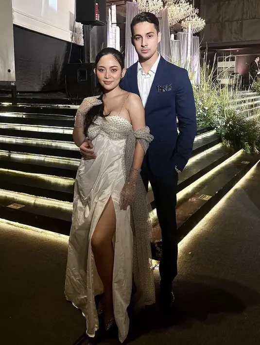 Untuk resepsi, ia mengenakan slit dress satin berdada rendah. Ditambah aksen kain motif polkadot di bagian dada hingga ke satu sisi lengannya.   (@rachelvennya)
