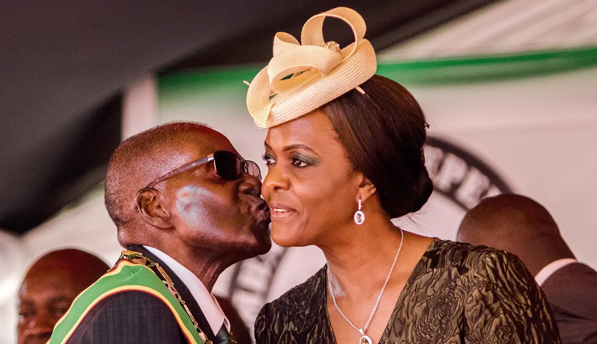 Presiden Zimbabwe, Robert Mugabe mencium istrinya Grace Mugabe saat perayaan Hari Kemerdekaan ke-37 negaranya di Stadion Olahraga Nasional di Harare (18/3). Polisi telah menyelidiki dugaan serangan Grace Mugabe. (AFP Photo/Jekesai Njikizana)