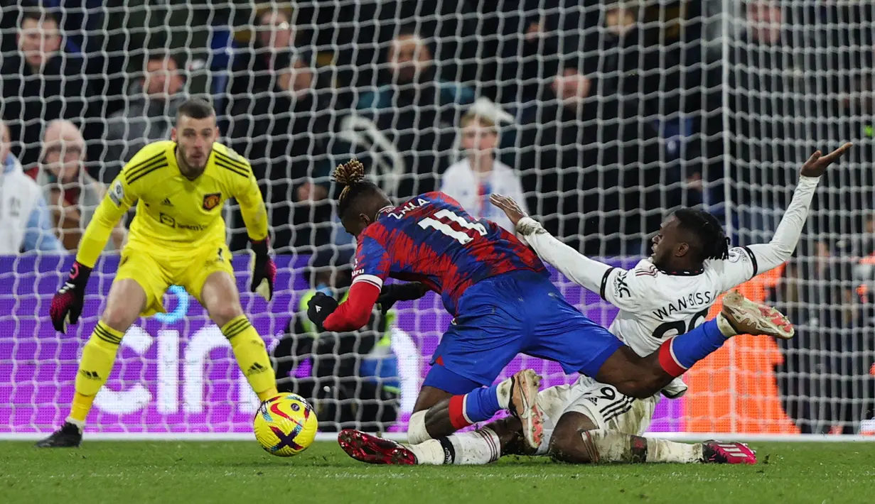 Bek Manchester United (MU) Aaron Wan-Bissaka menjegal striker Crystal Palace Wilfried Zaha (tengah) saat ia berlari dengan bola ke arah gawang pada matchday 19 Liga Inggris di Stadion Selhurst Park, London, Kamis dini hari WIB (19/1/2023). Sementara, Crystal Palace ada di posisi 12 dengan 23 poin. (ADRIAN DENNIS / AFP)