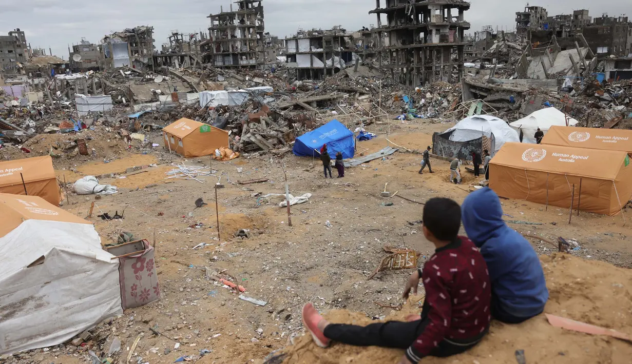 Anak-anak Palestina yang mengungsi duduk di atas gundukan pasir yang menghadap ke tenda-tenda yang didirikan di tengah-tengah bangunan yang hancur di Jabalia, Jalur Gaza utara pada 6 Februari 2025, saat gencatan senjata dalam perang antara Israel dan Hamas. (Bashar TALEB/AFP)