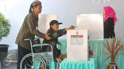 Warga disabilitas dibantu petugas KPPS berpakaian tradisional khas Jawa dan blangkon saat mengikuti pencoblosan Pilkada DKI 2017 di TPS tempat Presiden Jokowi menggunakan hak suaranya, TPS 04 Gambir, Jakarta Pusat, Rabu (15/2). (Liputan6.com/Angga Yuniar)