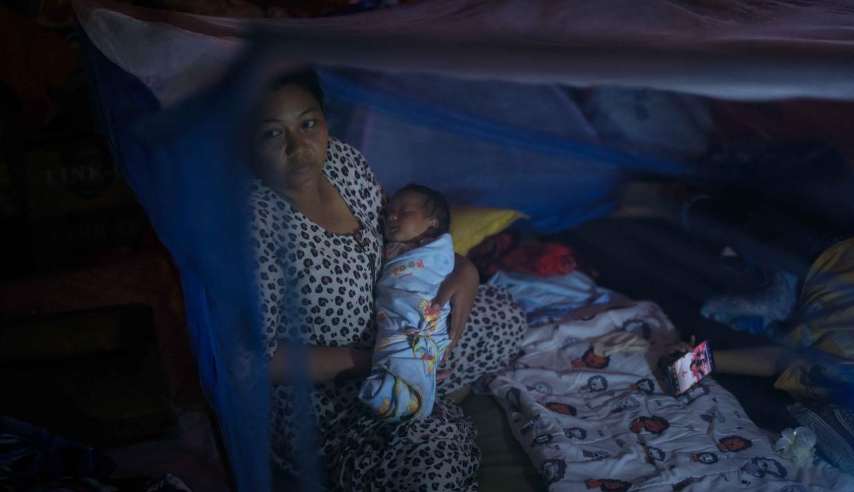 Beberapa kawasan permukiman warga yang kini mengungsi di tenda-tenda darurat dilaporkan masih gelap gulita. Tampak dalam foto, Lia Minarti, 35 tahun, menggendong bayinya, Muhammad Hafid, yang hampir berusia satu bulan, di dalam kelambu di tenda darurat setelah kehilangan rumahnya akibat banjir bandang sekitar tiga minggu sebelumnya, di Aceh Tamiang, pada Selasa 16 Desember 2025. (Yasuyoshi Chiba/AFP)