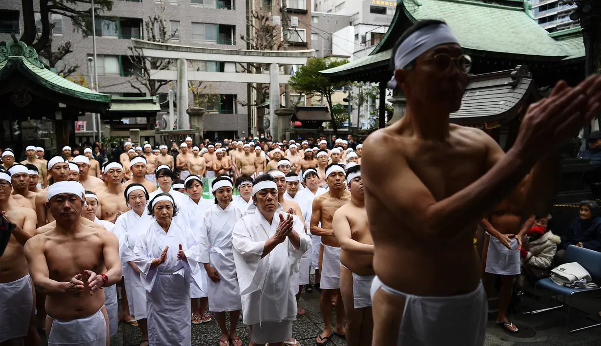 Orang-orang percaya Shinto dari Kuil Teppozu Inari berdoa sebelum mandi dengan air dingin untuk memurnikan jiwa dan tubuh mereka selama ritual Tahun Baru di Tokyo (12/1/2020). Sekitar 100 orang percaya Shinto ambil bagian dalam ritual tahunan tersebut. (AFP/Charly Triballeau)