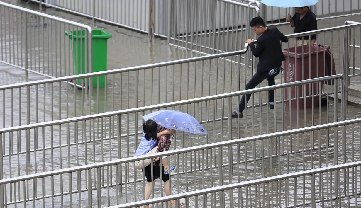 Sejumlah orang berjalan di atas pagar untuk mencoba menyebrang jalan yang terkena banjir, Shanghai, Tiongkok, Senin (24/8/2015). Banjir disebabkan oleh hujan deras yang menimpa kawasan tersebut. (Reuters/Aly Lagu)