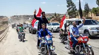 Pengendara motor mengibarkan bendera Suriah saat melintasi jalan raya utama antara Homs dan Hama yang dibuka kembali, Rabu (6/6). Pemerintah Suriah membuka kembali jalan raya Homs-Hama setelah ditutup selama hampir tujuh tahun. (AFP/STRINGER)