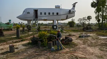 Foto yang diambil pada 12 Maret 2023 ini memperlihatkan Chrach Peou sedang menyemprotkan air di taman depan rumahnya yang berbentuk pesawat terbang di provinsi Siem Reap, Kamboja. (Photo by TANG CHHIN SOTHY / AFP)