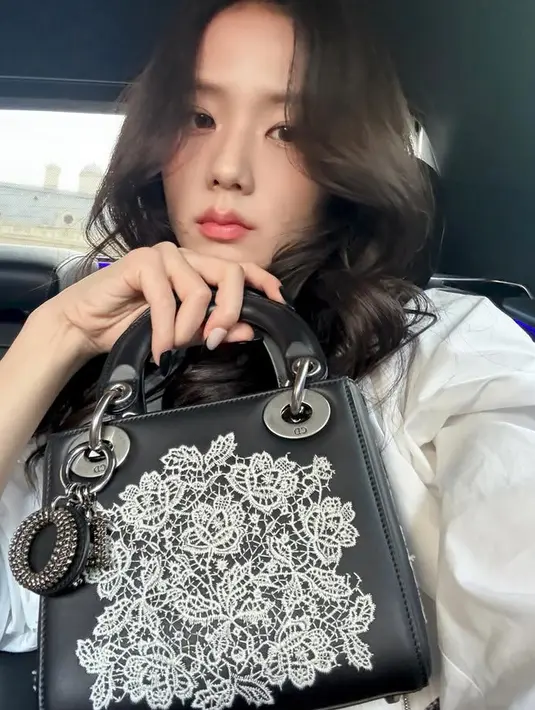 Jisoo memamerkan tas Dior yang ia bawa. Kali ini ia membawa tas Dior model kotak warna hitam dengan lace di bagian depan warna putih motif floral. Dan memiliki keychain Diornya.  [@sooyaaa__]