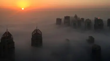 Pemandangan saat matahari terbit memancarkan sinar yang berwarna oranye keemasan diantara gedung pencakar langit di Kota Dubai, Uni Emirat Arab, Senin (5/12). Telihat banyak dari puncak gedung-gedung itu menembus awan. (AFP/Rene Slama)