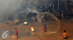 Beberapa warga berusaha menyiramkan air sungai saat terjadinya kebakaran yang melanda rumah hunian semi permanen di bantaran sungai anak kali ciliwung, Kawasan Kampung Berland, Jakarta, Rabu (2/9/2015). (Liputan6.com/Johan Tallo)
