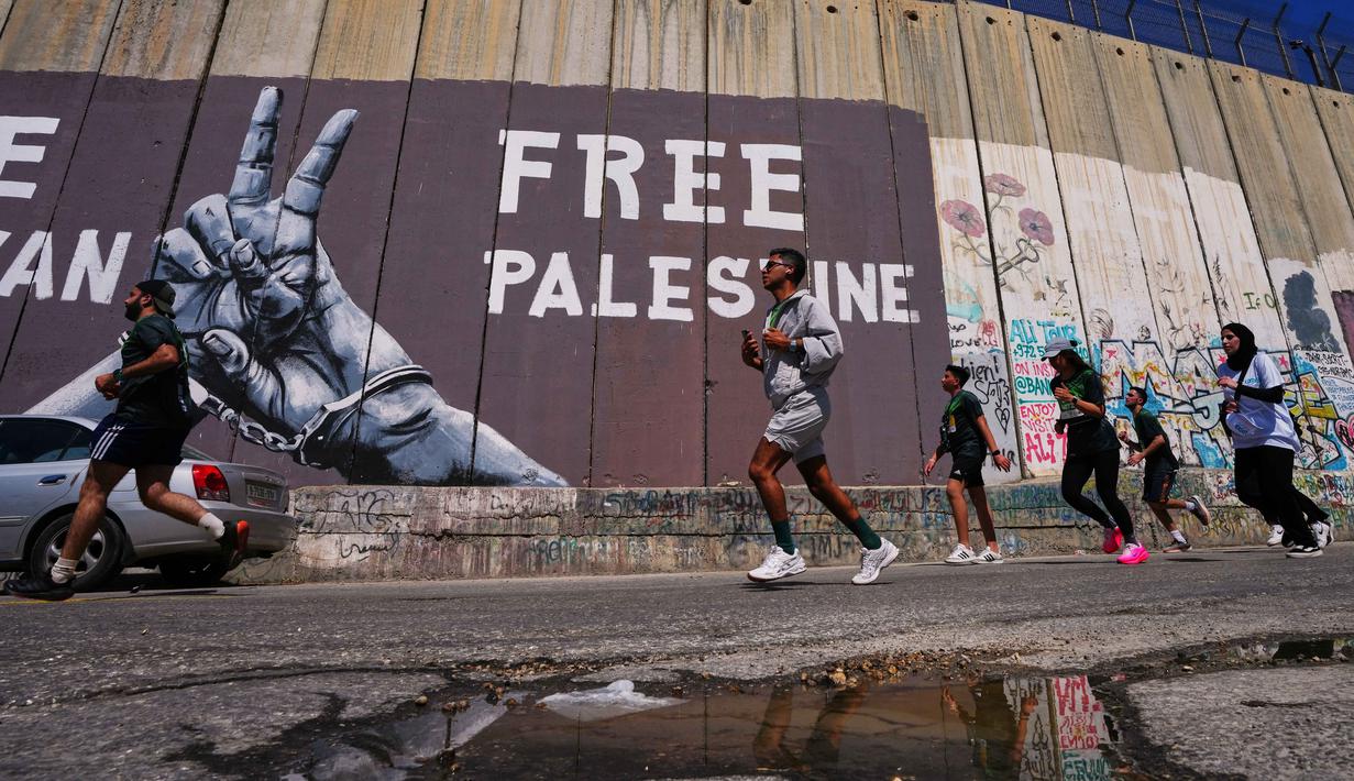 Para pelari melewati tembok pemisah Israel saat mereka berkompetisi dalam Maraton Palestina di kota Betlehem, Tepi Barat, Jumat 8 Mei 2026. Maraton Internasional Palestina kembali dilaksanakan pada Jumat 8 Mei 2026, di kota Betlehem, Tepi Barat. (AP Photo/Mahmoud Illean)