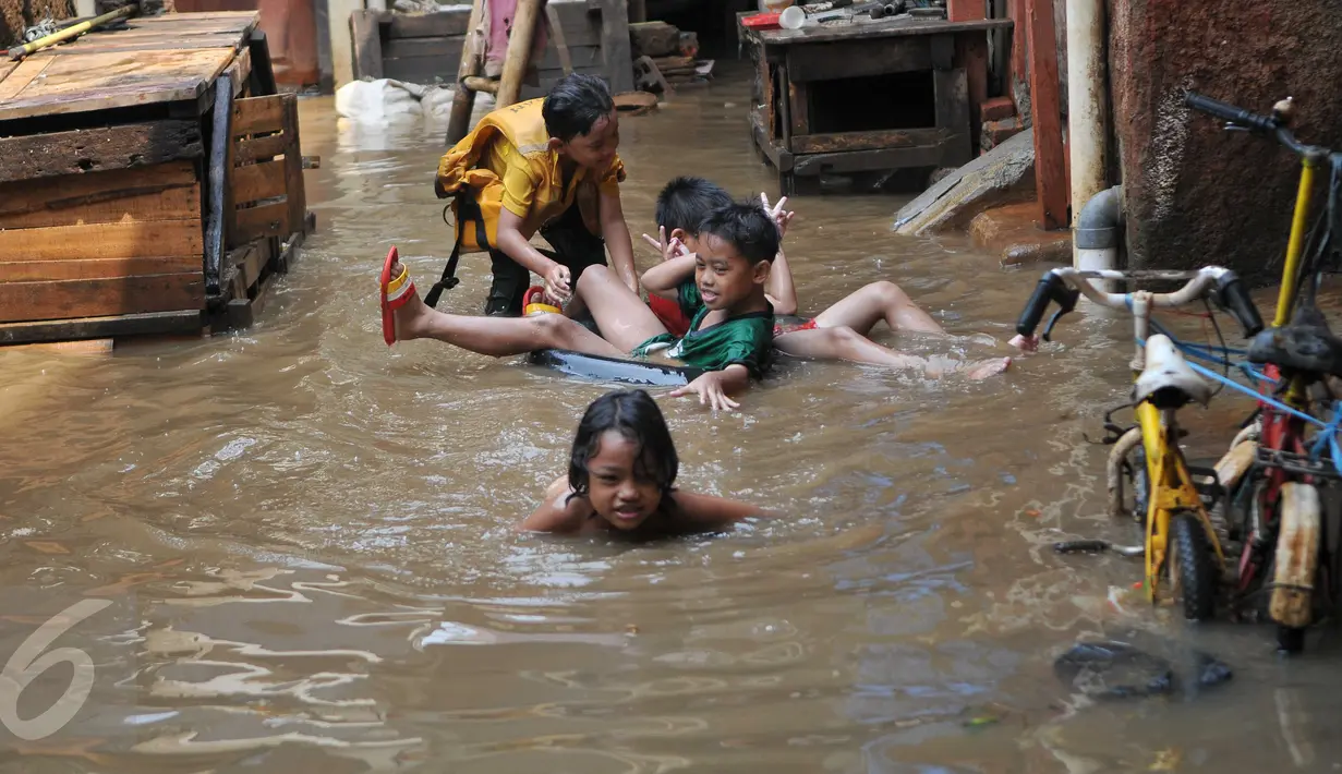 Anak-anak bermain di lokasi banjir yang merendam kawasan Kampung Pulo, Jakarta, Selasa (17/11). Kawasan di sepanjang aliran Kali Ciliwung terendam banjir sejak kemarin akibat Bendungan Katulampa yang sudah mencapai siaga satu (Liputan6.com/Gempur M Surya)