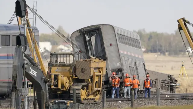 Para pekerja berjalan pada Minggu, 26 September 2021, di samping kereta Amtrak yang tergelincir pada Sabtu di sebelah barat Joplin, Montana (AP Photo)