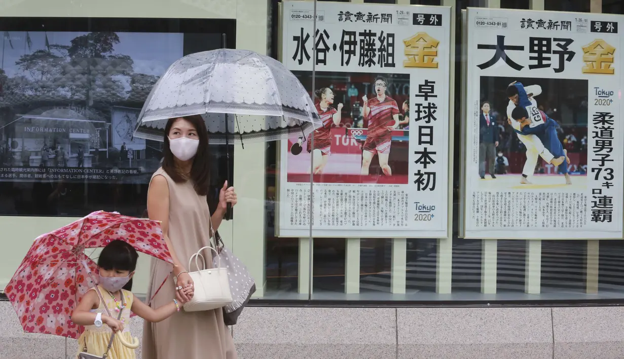 Warga Jepang mengenakan masker berjalan melewati poster yang berisi informasi peraih medali emas dari Jepang di Olimpiade Tokyo, Selasa (27/7/2021). (Foto: AP/Koji Sasahara)