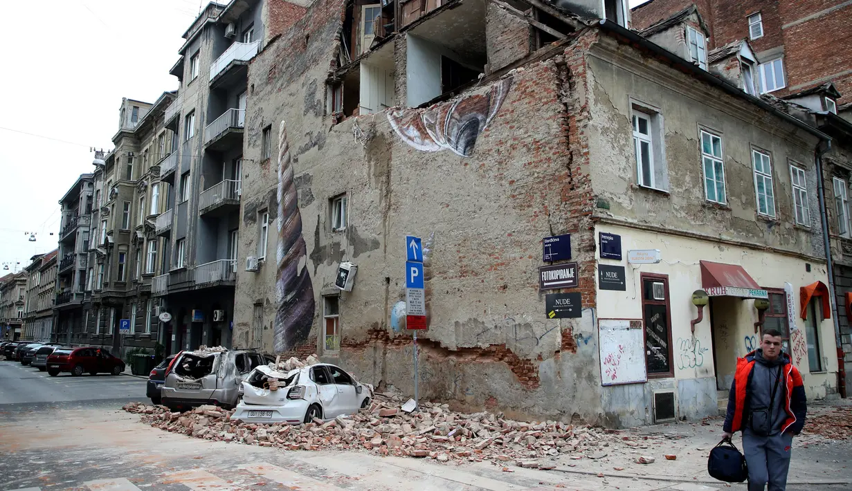 Gempa Terparah dalam 140 Tahun di Kroasia: Warga melewati bangunan yang rusak dan mobil-mobil hancur oleh puing-puing setelah gempa di jalan-jalan pusat kota Zagreb (22/3/2020).  Gempa magnitudo 5,3 ini tercatat sebagai yang terbesar, yang mempengaruhi Kroasia dalam 140 tahun. (AFP/Damir Sencar)