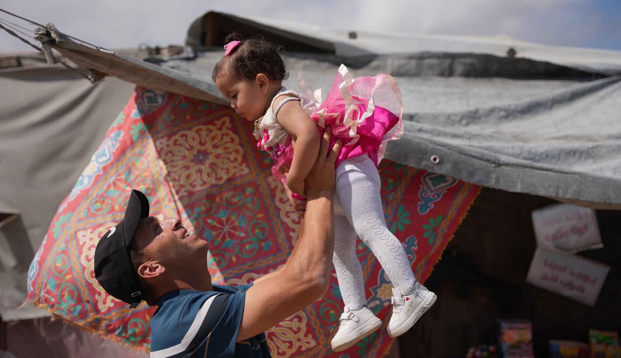 Abdullah Al-Hurkali bermain dengan putrinya, Tasneem, selama Hari Raya Idul Adha di sebuah kamp tenda untuk pengungsi Palestina di Khan Younis, Jalur Gaza, Rabu 27 Mei 2026. (AP Photo/Abdel Kareem Hana)