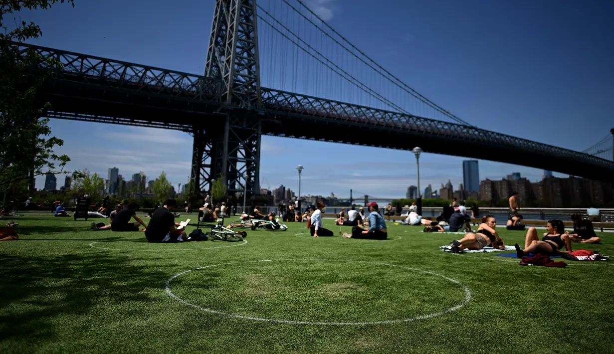 Orang-orang berusaha menjaga jarak dalam lingkaran putih saat bersantai di Domino Park, Brooklyn di Kota New York, Minggu (17/5/2020). Pengunjung taman berjemur dengan tetap menerapkan protokol penularan coorna Covid-19. (Photo by Johannes EISELE / AFP)
