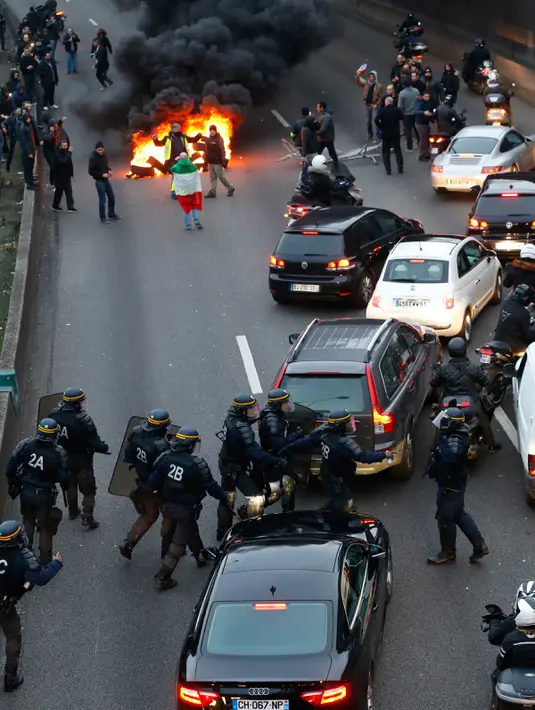 Polisi anti huru-hara tiba ketika pengemudi taksi memblokir jalan dengan membakar ban saat unjuk rasa menentang layanan transportasi VTC seperti Uber, di jalan lingkar di porte Maillot di Paris, Perancis, Selasa (26/1). (AFP PHOTO/Thomas SAMSON)