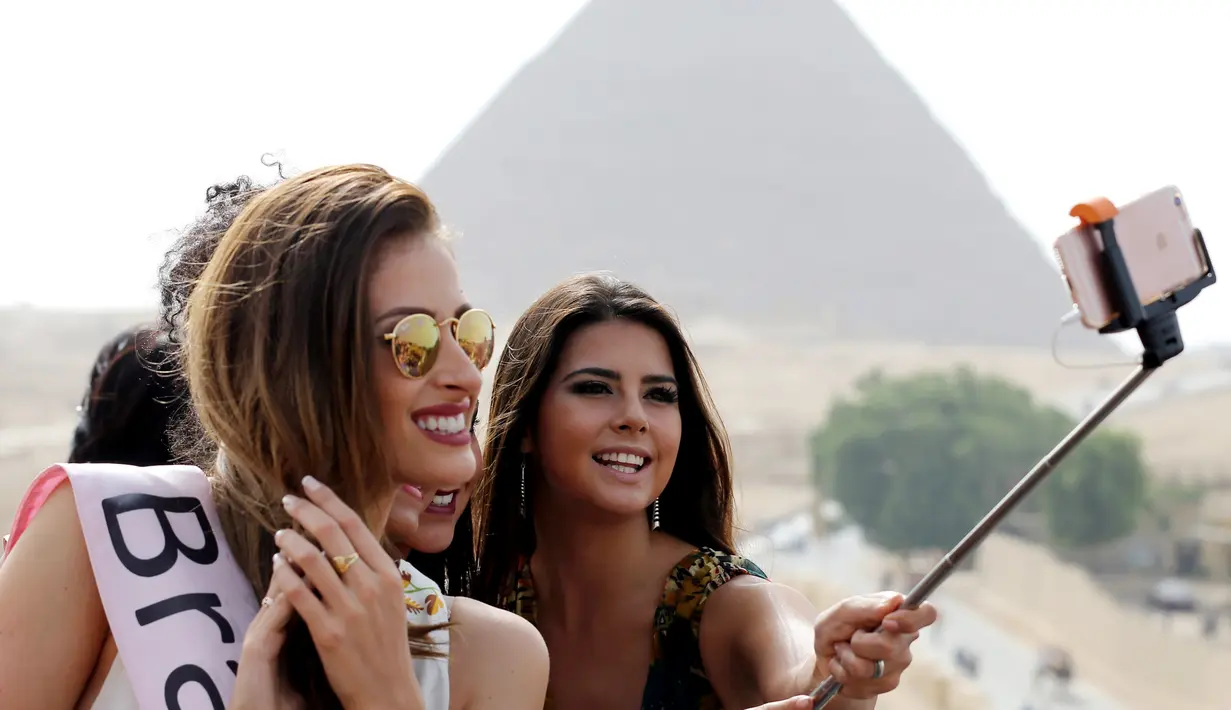 Kontestan Miss ECO Universe berselfie menggunakan tongsis dengan latar belakang segitiga piramida di pinggiran Kairo, Mesir (10/4). Pemenang Miss Eco Universe 2016 akan memenangkan hadiah uang tunai USD 10.000. (REUTERS/Mohamed Abd El Ghany)