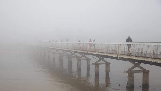Pejalan kaki menyeberangi jembatan saat hari berkabut di Tel Aviv, Israel, Rabu (6/1/2021). Kabut yang cukup tebal tersebut disebabkan oleh udara yang mengalir ke darat dari laut, menyebabkan kelembaban meningkat di dataran pantai dan daerah lainnya. (AP Photo/Oded Balilty)