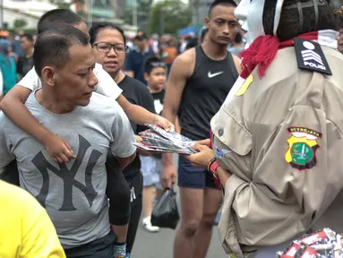 Petugas bersama ondel-ondel membagikan brosur sosialisasi E-Tilang saat car free day di bunderan HI, Jakarta, Minggu (28/10). Kegiatan sosialisasi E-Tilang tersebut agar masyarakat lebih mengetahui sanksi yang akan diberikan. (Liputan6.com/Faizal Fanani)