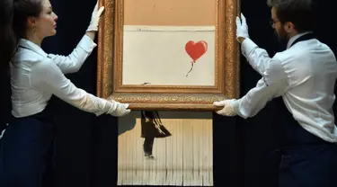 Karyawan berpose dengan lukisan "Girl with Balloon" di rumah lelang Sotheby London, 12 Oktober 2018. Lukisan karya seniman Bansky itu rusak menjadi potongan-potongan saat terjual seharga sekitar Rp 20 miliar pada lelang 5 Oktober 2018. (BEN STANSALL/AFP)