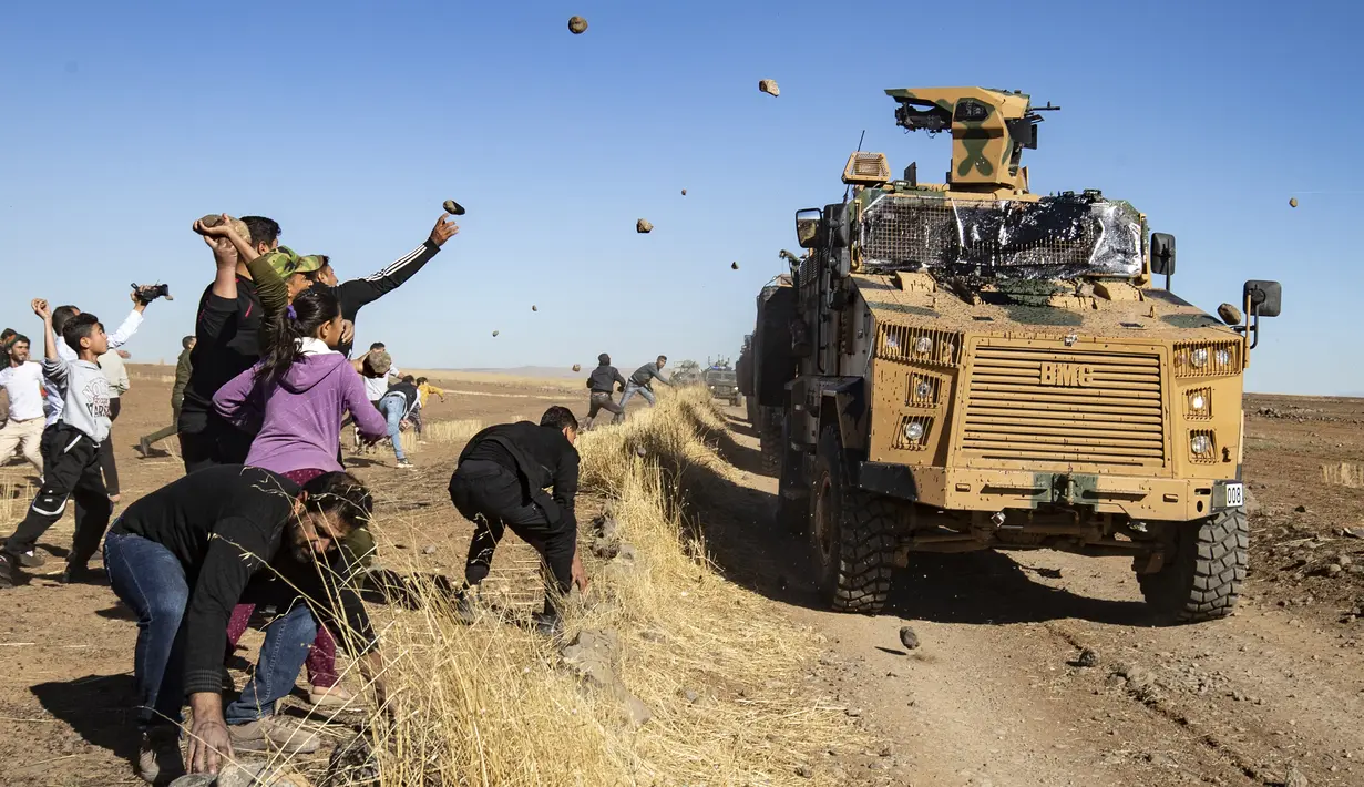 Sejumlah warga Kurdi melemparkan batu ke kendaraan militer Turki di dekat kota Al-Muabbadah, bagian timur laut Hassakah, Suriah (8/11/2019). Pelemparan batu terjadi saat militer Turki melakukan konvoi dengan militer Rusia. (AFP/Delil Souleiman)