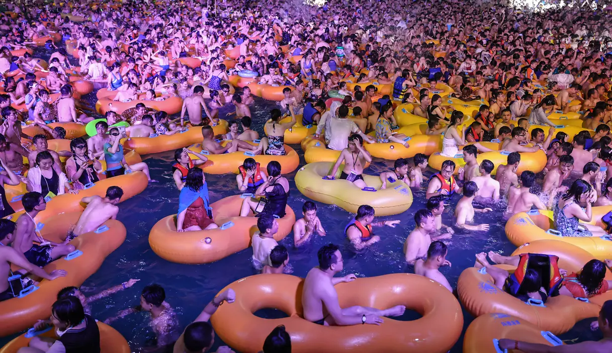 Foto pada 15 Agustus 2020 memperlihatkan orang-orang menonton pertunjukan musik sambil bermain air di sebuah taman air atau water park di Wuhan, provinsi Hubei, China. Mereka berpesta saat Wuhan kembali ke kehidupan normal setelah sempat terdampak parah oleh COVID-19. (STR/AFP)