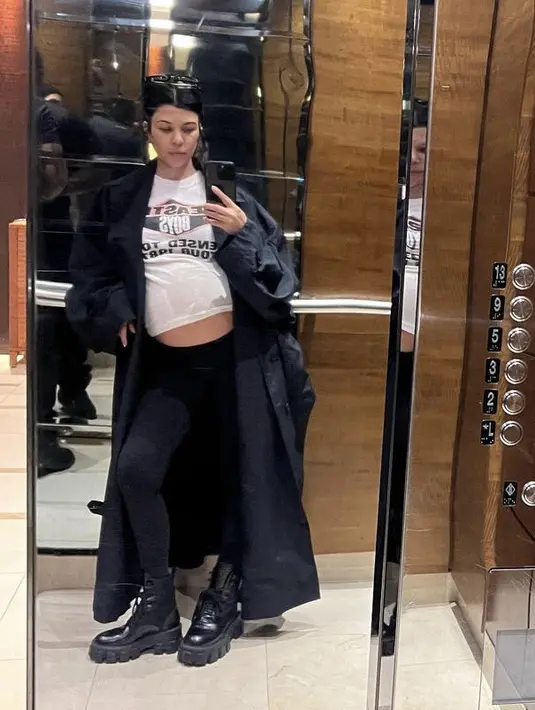 Mengenakan coat panjang hitam serasi dengan legging dan bootsnya, Kourtney memerlihatkan baby pumpnya dengan t shirt coat putih Beastie Boys.  @kourtneykardash