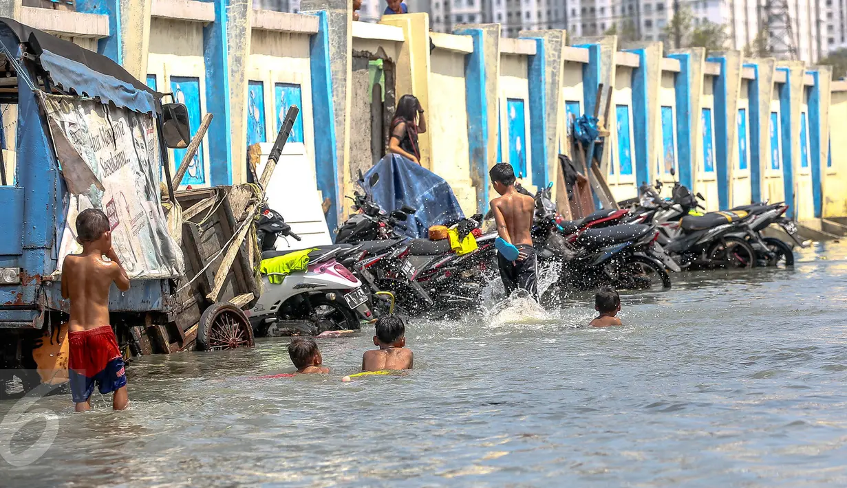 Sejumlah anak bermain genangan air banjir rob di kawasan akses pintu masuk menuju pelabuhan Kali Adem, Muara Angke, Jakarta, Senin (2/1). (Liputan6.com/Faizal Fanani)