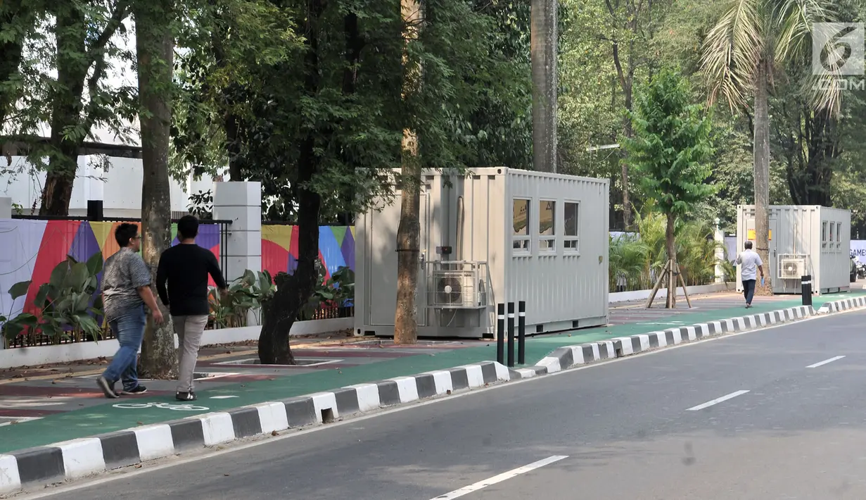 Pejalan kaki melintas di depan kontainer tiket Asian Games 2018 yang berdiri di sepanjang trotoar Jalan Pintu 1 Senayan, Jakarta, Selasa (7/8). Langkah Panitia Penyelenggara Asian Games 2018 (INASGOC) ini menuai kritik. (Merdeka.com/Iqbal Nugroho)