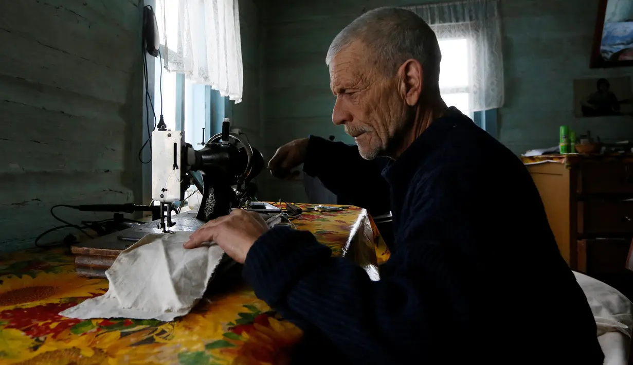 Mikhail Baburin (66) menggunakan mesin jahit di rumahnya di desa Mikhailovka di Siberia, 5 Desember 2016. Selama 10 tahun terakhir, Baburin tinggal sendirian di desa yang letaknya sangat terpencil. (REUTERS/Ilya Naymushin)
