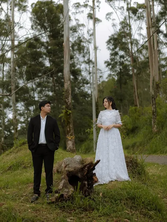 Salah satu foto memperlihatkan Frans dan Indah berada di hutan dengan pepohonan tinggi yang menjulang. Indah tampil anggun dalam gaun putih beraksen renda yang memancarkan kesan klasik, sedangkan Frans mengenakan setelan jas hitam dengan kemeja putih, tampil rapi dan elegan. Komposisi kayu besar di latar depan menambah elemen artistik sekaligus menciptakan kesan alami yang tenang. (Liputan6.com/IG/@fransfaisal_)