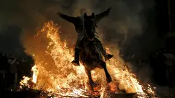 Seorang pria mengendarai kuda melintas kobaran api selama perayaan " Luminarias " di desa San Bartolome de Pinare, Spanyol, (16/1).  Dulunya tradisi ini untuk mengawetkan hewan - hewan menggunakan api unggun. (REUTERS / Susana Vera)