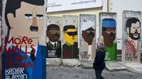 Seorang gadis melihat-lihat bekas Tembok Berlin yang digambari dengan karikatur para pemimpin dunia. Graffiti itu dilukis oleh artis Prancis Guillaume Kashima, dekat Checkpoint Charlie di Berlin, Jerman, 13 Januari 2013. (John MacDougall/AFP)