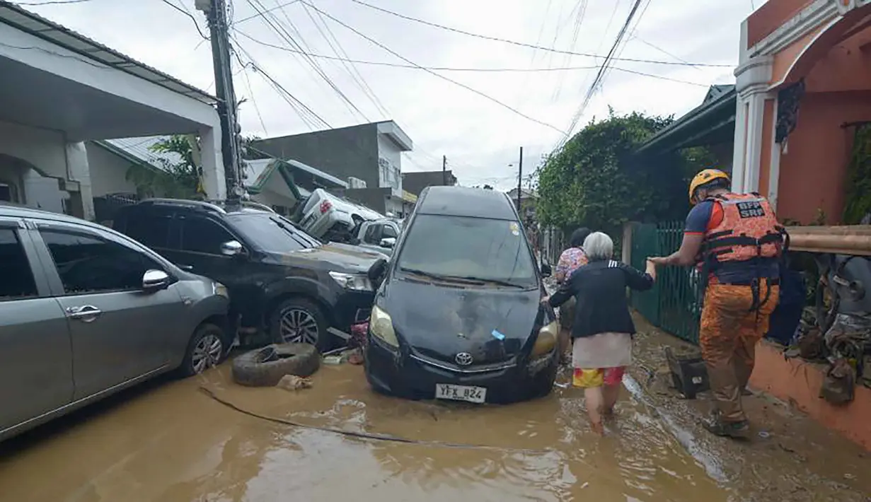 Seorang petugas penyelamat membantu warga saat mereka berjalan melewati mobil-mobil yang tersapu banjir pada puncak Topan Kalmaegi di sebuah permukiman di Kota Cebu, Filipina tengah, pada Selasa 4 November 2025. Sejumlah warga dilaporkan terjebak di atap rumah akibat naiknya air, sementara puluhan kendaraan terendam. (Alan TANGCAWAN/AFP)